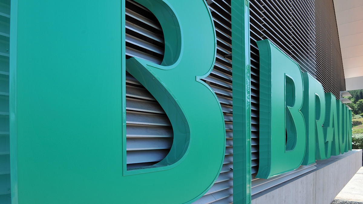 Close de um logotipo tridimensional da B. Braun na fachada de um edifício moderno