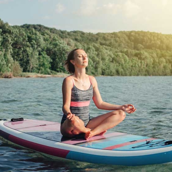 mulher jovem meditando em uma prancha de stand-up paddle