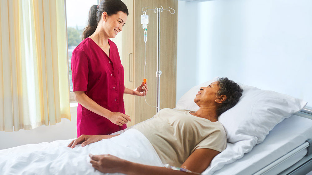 Enfermeira com ecoflac plus em um suporte de infusão conversando com um paciente deitado na cama