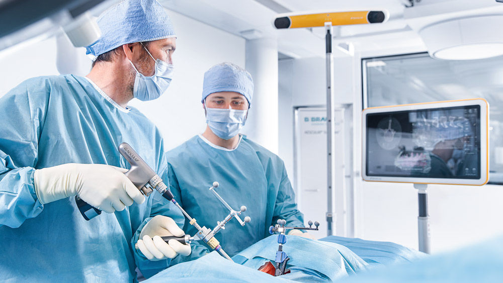 Dois cirurgiões na sala de cirurgia usando um equipamento de navegação espinhal durante um procedimento cirúrgico