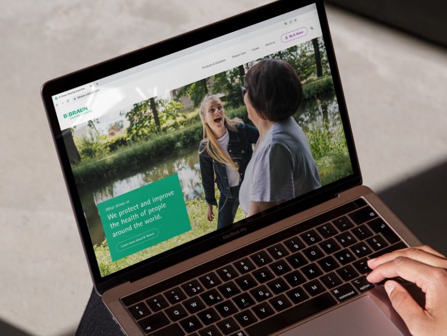 Um laptop com o site da B. Braun aberto e uma mão apoiada no canto inferior direito do laptop. 