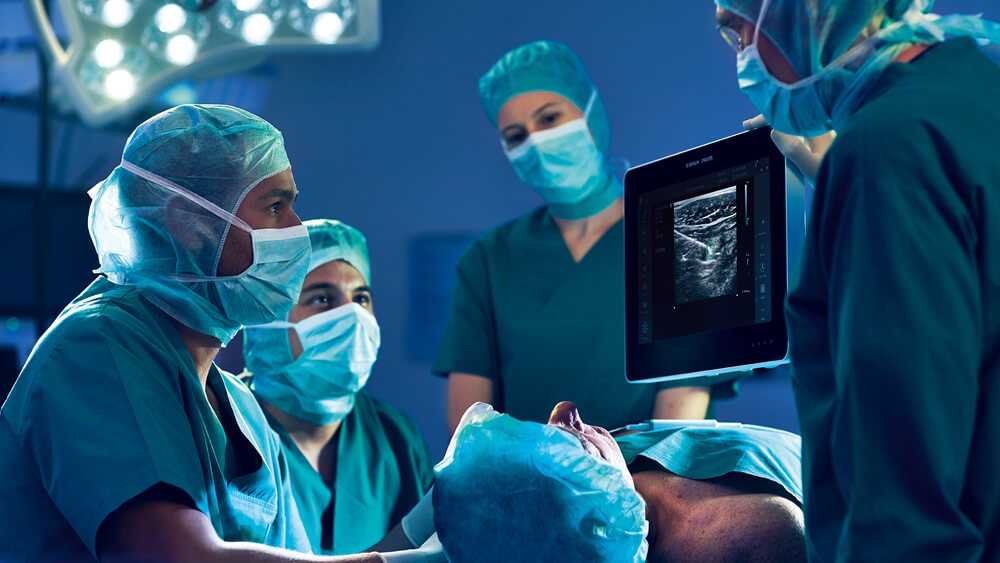 A equipe médica observa um bloqueio do plexo infraclavicular guiado por ultrassom em um monitor na sala de cirurgia