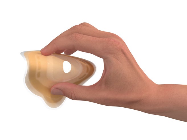Uma mão pressiona a placa de uma bolsa de estoma convexa e macia para demonstrar sua flexibilidade