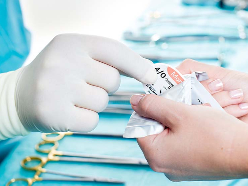 Mãos de um profissional de saúde segurando um pequeno curativo adesivo para tratamento de feridas