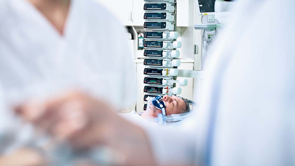 Paciente deitado em uma unidade de terapia intensiva - há muitas bombas de infusão da B. Braun ao fundo