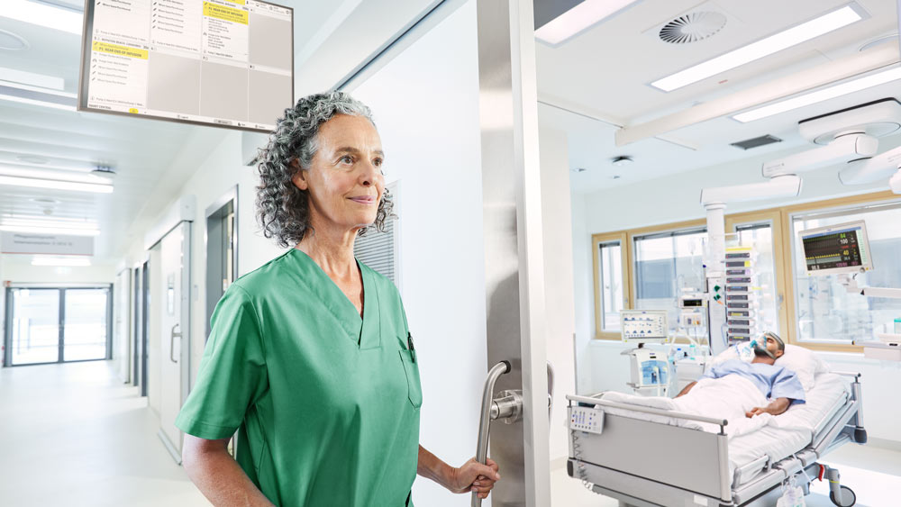 Enfermeira no corredor do hospital, equipado com UTI silenciosa - no quarto está um paciente na unidade de terapia intensiva