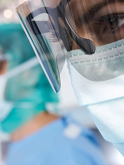 Médica usando máscara e óculos especiais, parecendo preocupada enquanto observa um procedimento