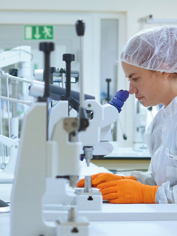 Uma profissional de saúde senta-se à mesa, analisando amostras através de um microscópio médico