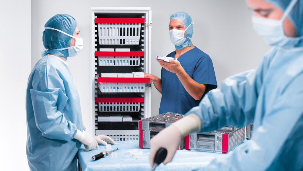 Três profissionais de saúde, vestidos com uniformes médicos e máscaras, estão colaborando em uma sala médica totalmente equipada