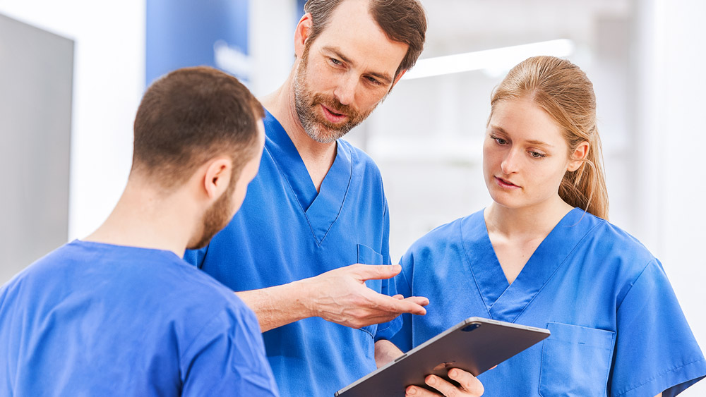 Três médicos discutem algo em um tablet