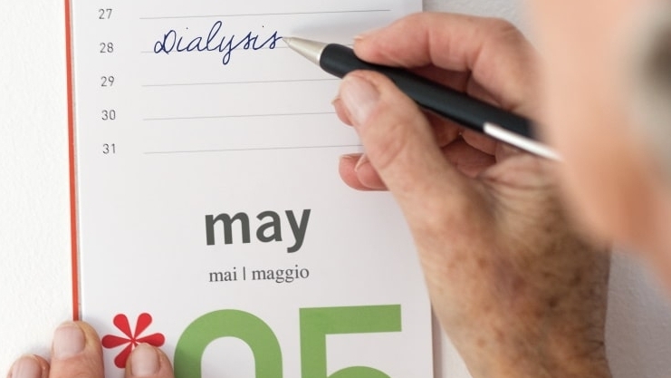 Uma mão escreve diálise em um calendário por 28 dias com uma caneta esferográfica