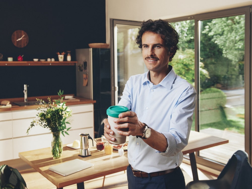 Um homem está em pé em uma casa particular, segurando uma xícara de café