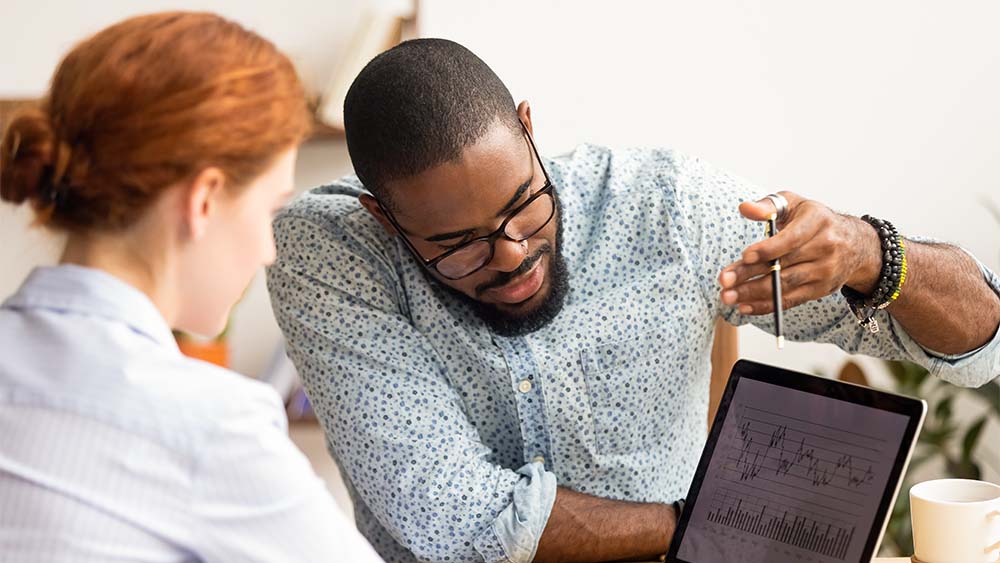 Duas pessoas discutindo gráficos e tabelas comerciais em um tablet em uma sala de escritório. 