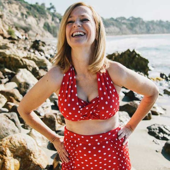 mulher na praia, rindo em biquíni vermelho com bolinhas brancas